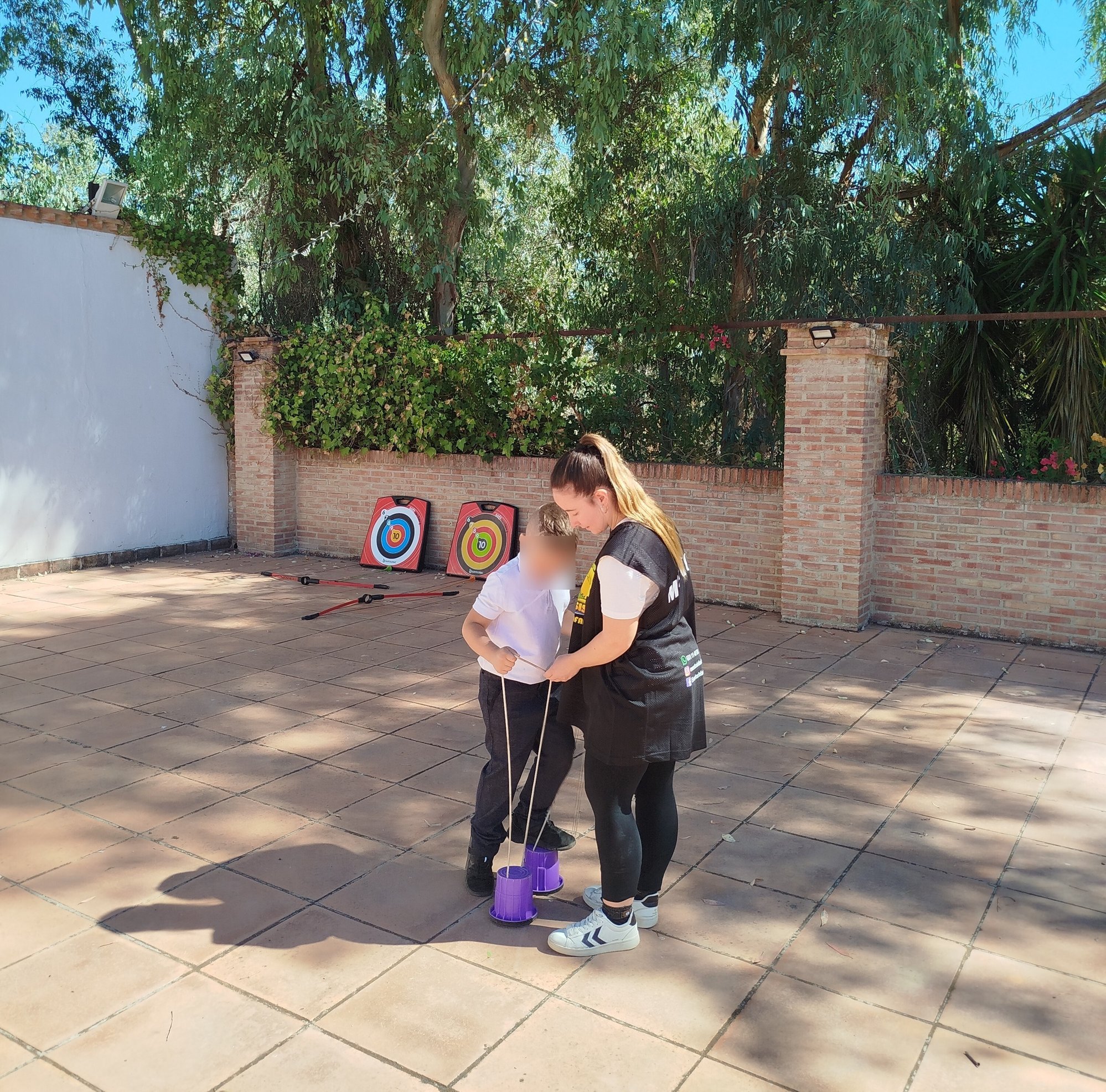 En esta imagen se puede ver una monitora infantil ayudando a un niño que quiere aprender a coger los zancos.